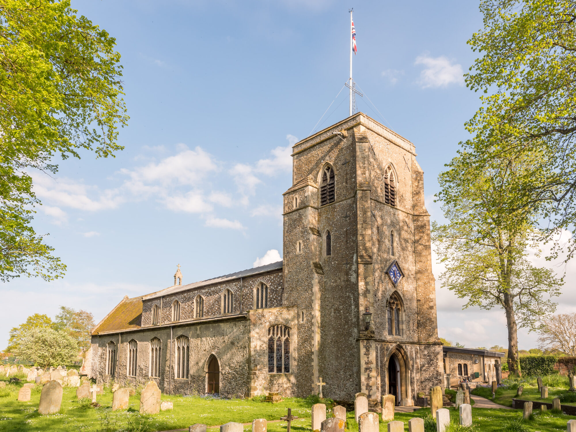 Photo of Holt St Andrew church, Holt taken on a sunny day. The union flag is raised.